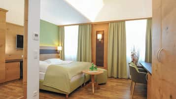 A hotel room with a bed, a small table with a bottle and glass, a chair, a desk, and a mirror.