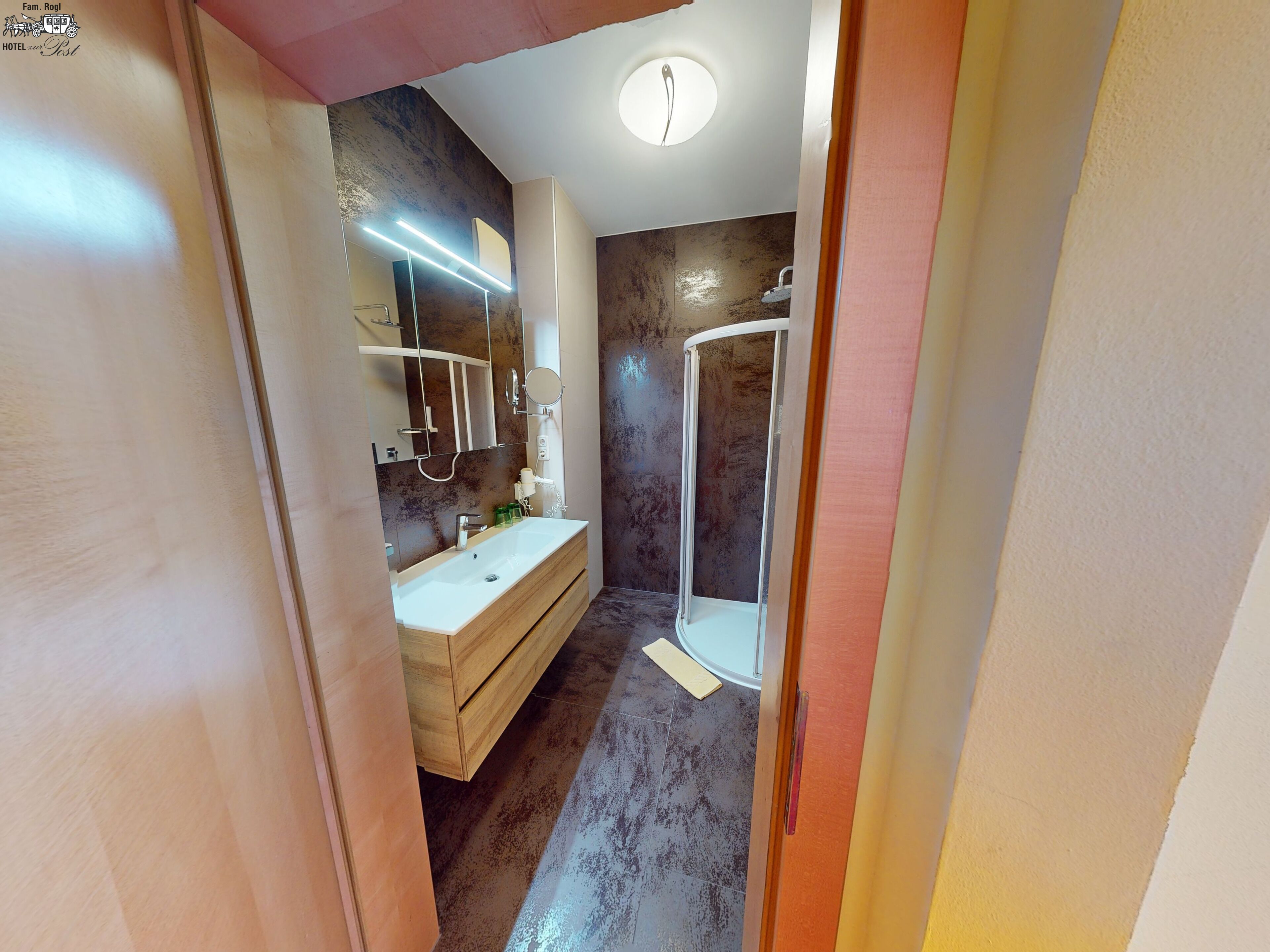A modern bathroom with a wooden vanity, a large mirror, and a walk-in shower.