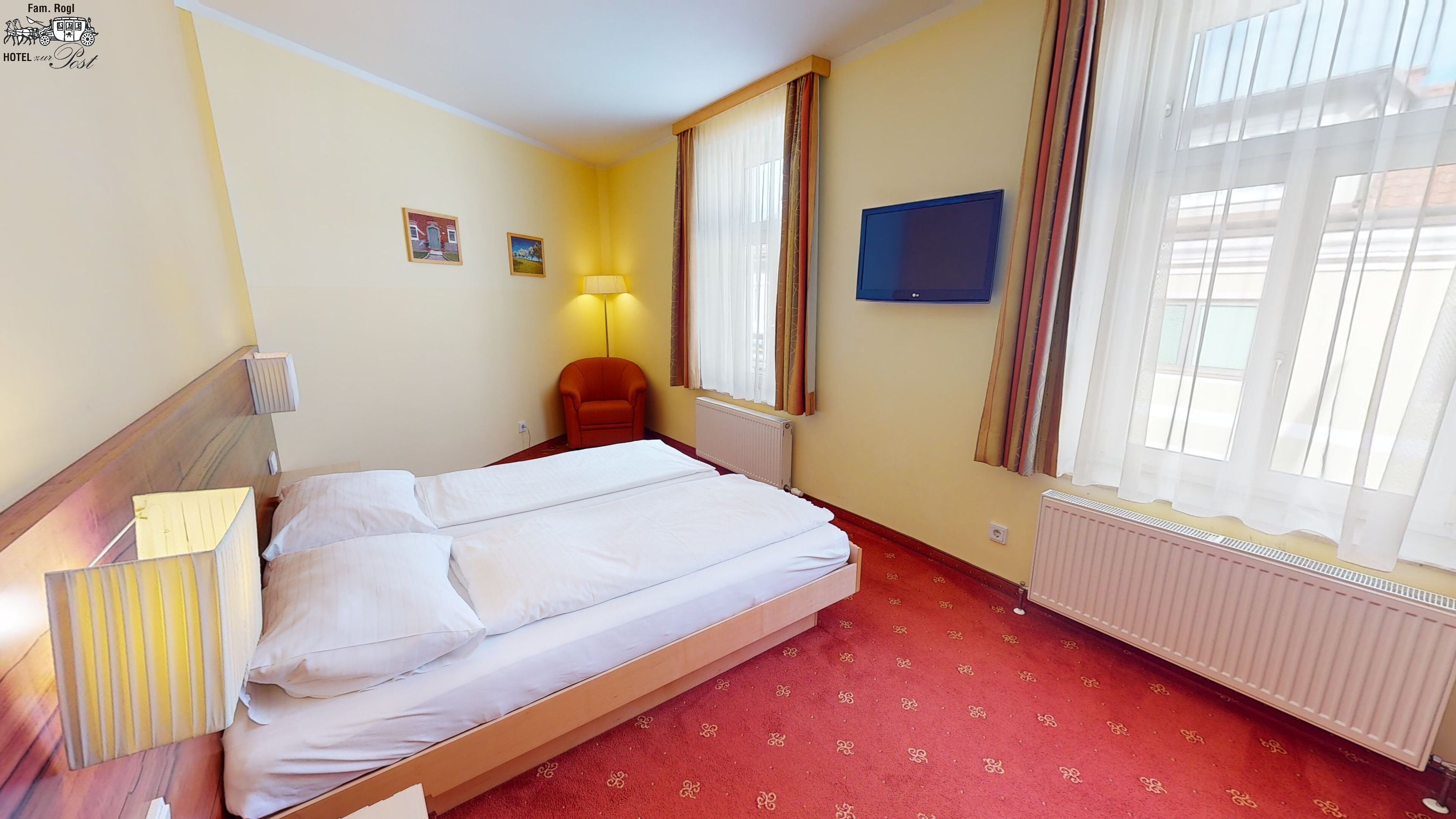 A hotel room with a bed, a chair, a TV, and a window with curtains.