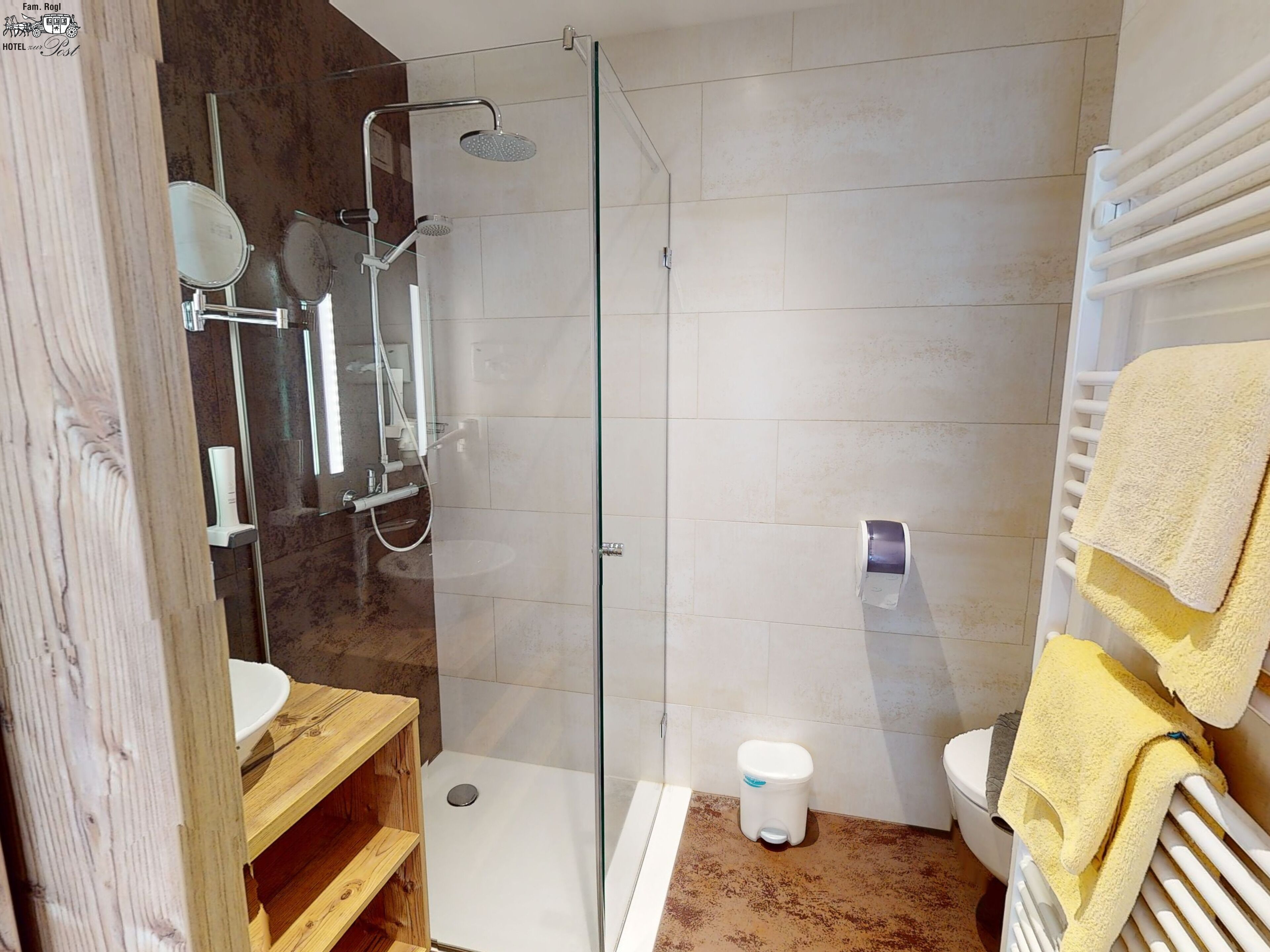 Un baño moderno con ducha acristalada, tocador de madera, inodoro y toallero con toallas amarillas.