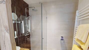 Un baño moderno con ducha acristalada, tocador de madera, inodoro y toallero con toallas amarillas.