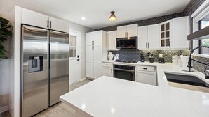 A modern kitchen with stainless steel appliances, white cabinetry, and a marble countertop. - Backyard Resort w/ Pool, Spa, Sauna + Theater (Austin)