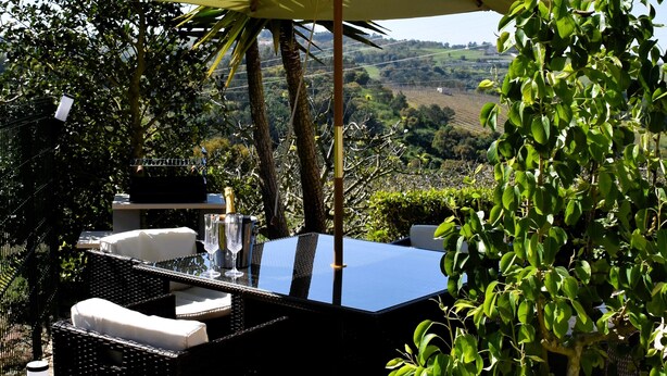 Ein Essbereich im Freien mit Tisch und Stühlen, einem großen Sonnenschirm und Blick auf die Landschaft.
