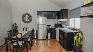 Cocina compacta con mesa, sillas, refrigerador, microondas, lavabo y alacenas.