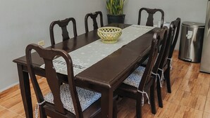Un comedor con una mesa rectangular, seis sillas, una planta en maceta y un cubo de basura.
