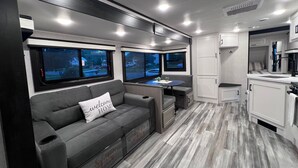 A modern RV interior with a sofa, a small table, and a kitchen area.