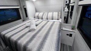 A modern, compact bedroom with a bed, a TV, and a small bedside table with a plant.