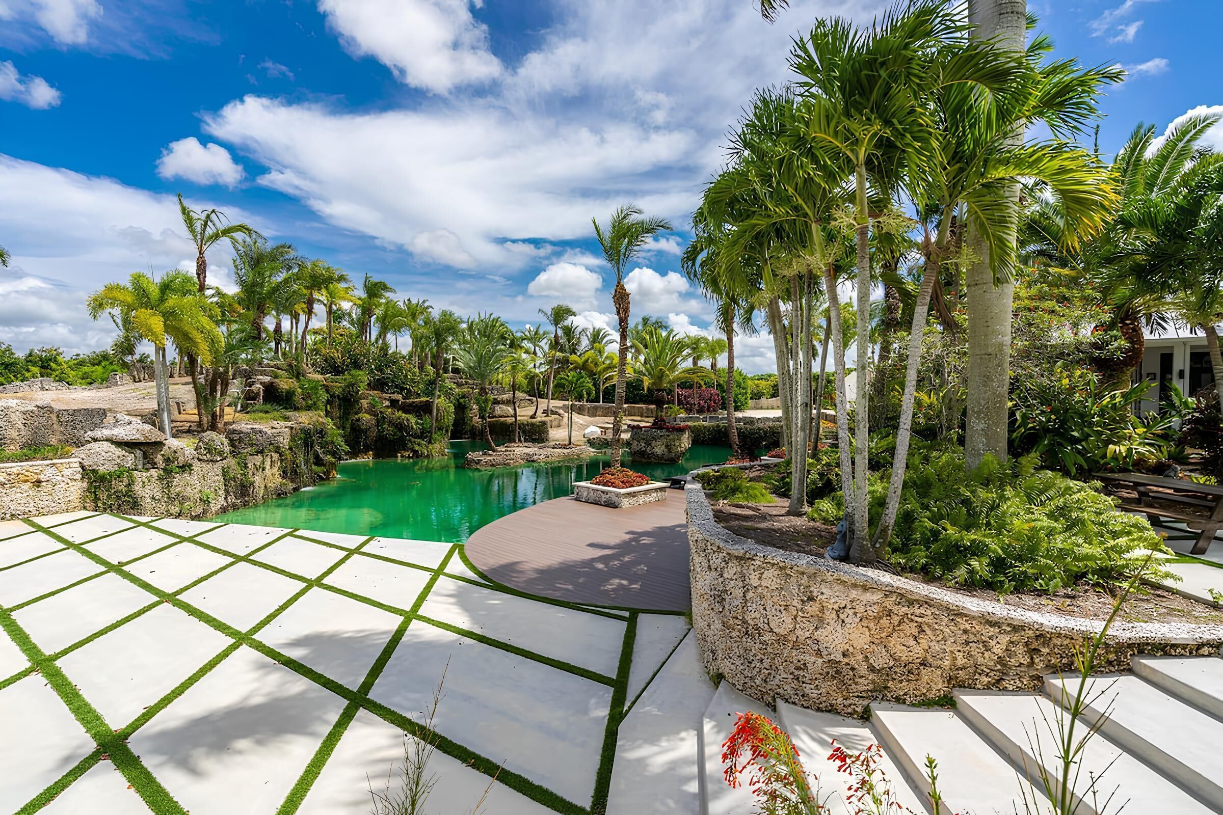 A resort pool area with a clear blue sky, palm trees, and a stone pathway.