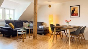 Una sala moderna con suelo de madera, un sofá gris oscuro, una mesita redonda y un comedor con mesa y sillas de madera.