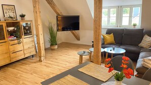 Una sala de estar moderna con un mueble de madera, un televisor de pantalla plana, un sofá gris y una mesa de comedor con individuales tejidos.