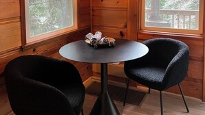Ein gemütlicher Raum mit Holzwänden, einem runden Tisch, zwei schwarzen Stühlen und einer Pendelleuchte.
