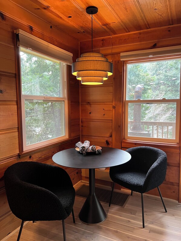 Una habitación acogedora con paredes de madera, una mesa redonda, dos sillas negras y una lámpara colgante.