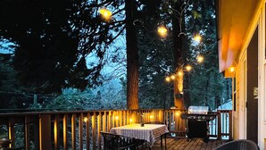 Eine Holzterrasse mit Tisch, Stühlen, Lichterketten und einem Grill.