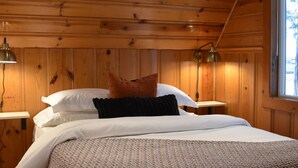 Ein Schlafzimmer in einer Holzhütte mit einem Bett, zwei Nachttischen und einem Fenster.