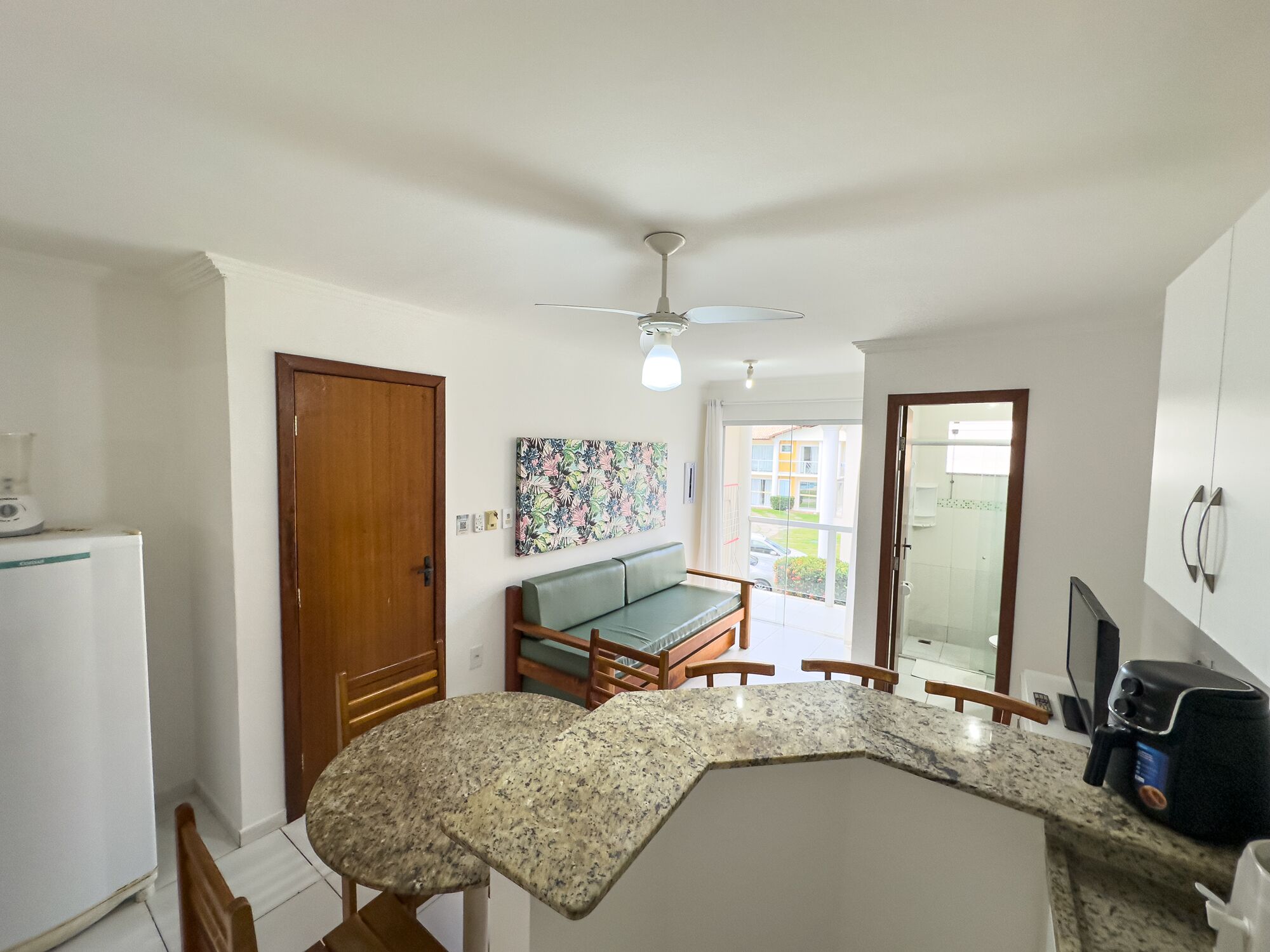Cocina compacta con encimera de granito, puerta de madera, ventilador de techo y vistas al balcón exterior.