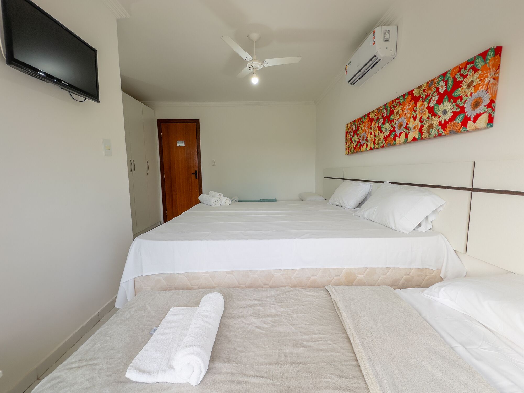 Ein Hotelzimmer mit Bett, Deckenventilator, Klimaanlage und Fernseher an der Wand.