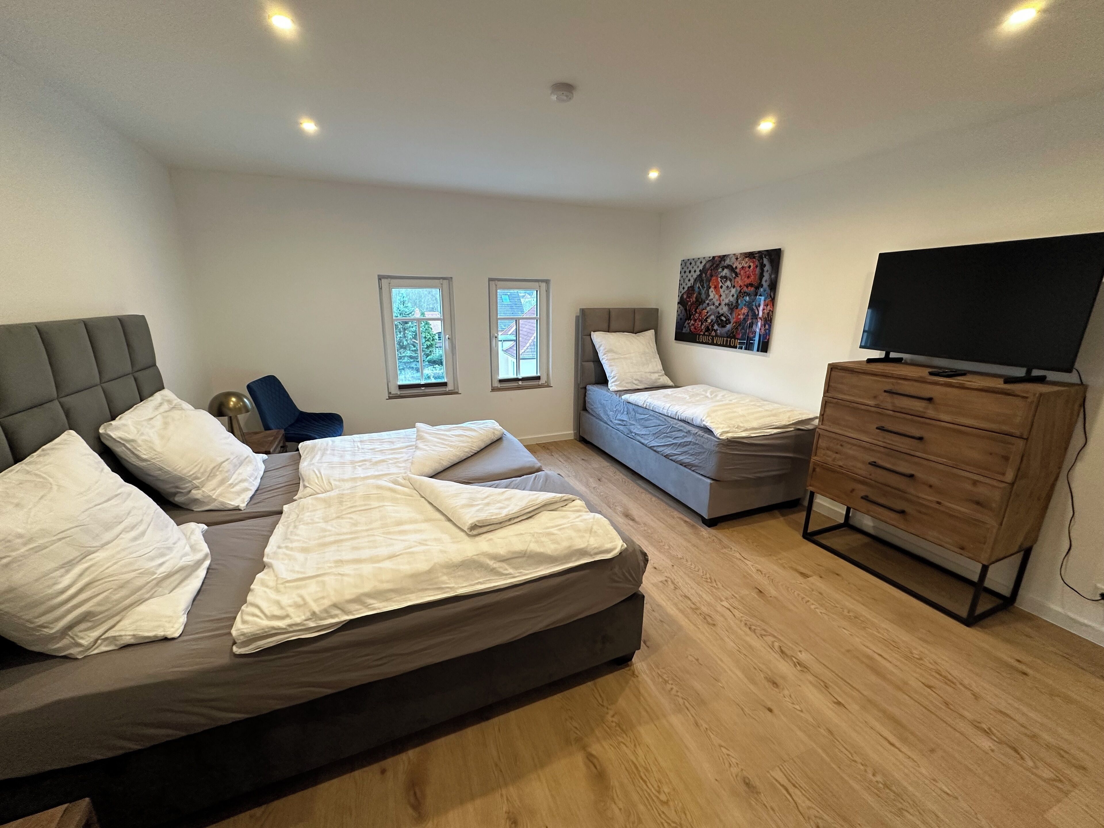 Une chambre avec deux lits, une commode, un téléviseur et deux fenêtres.