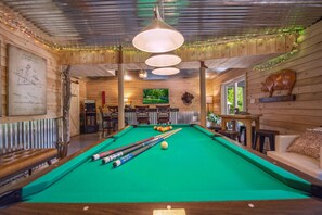 A pool table with balls, a sofa, and a television in a wooden room with a ceiling fan and string lights. - Trailblazer - hot tub, trail, game room, pets, wifi, fire pit, view, secluded (Berkeley Springs)