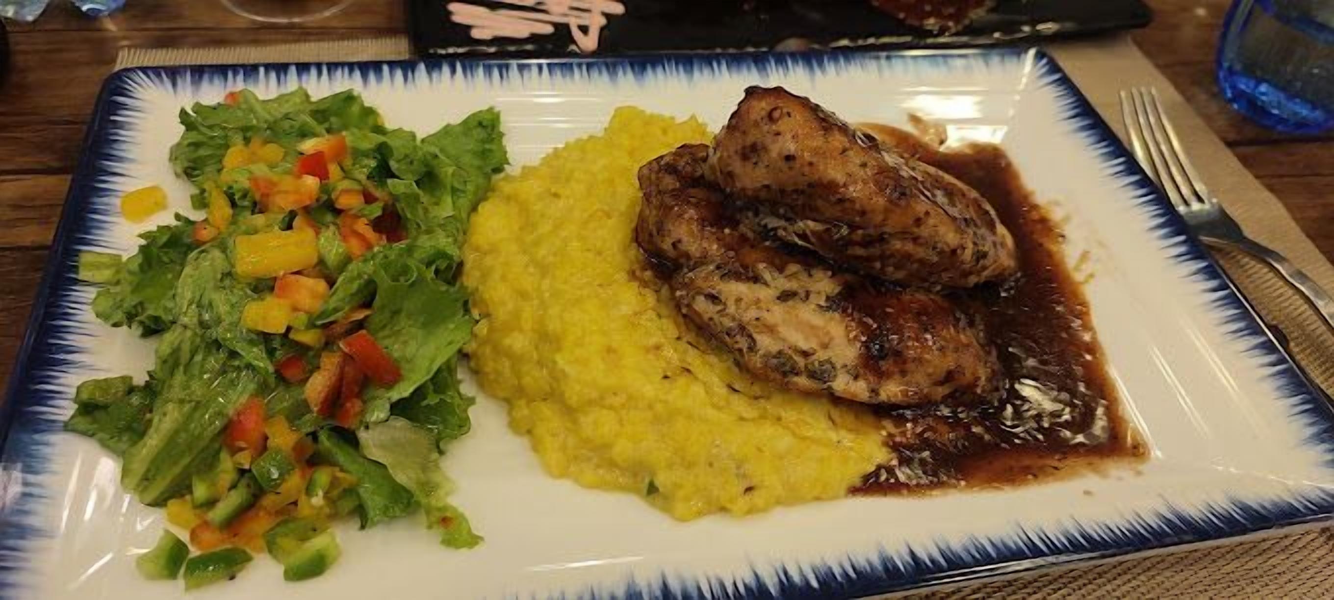 A plate with grilled chicken, yellow risotto, and a mixed vegetable salad.