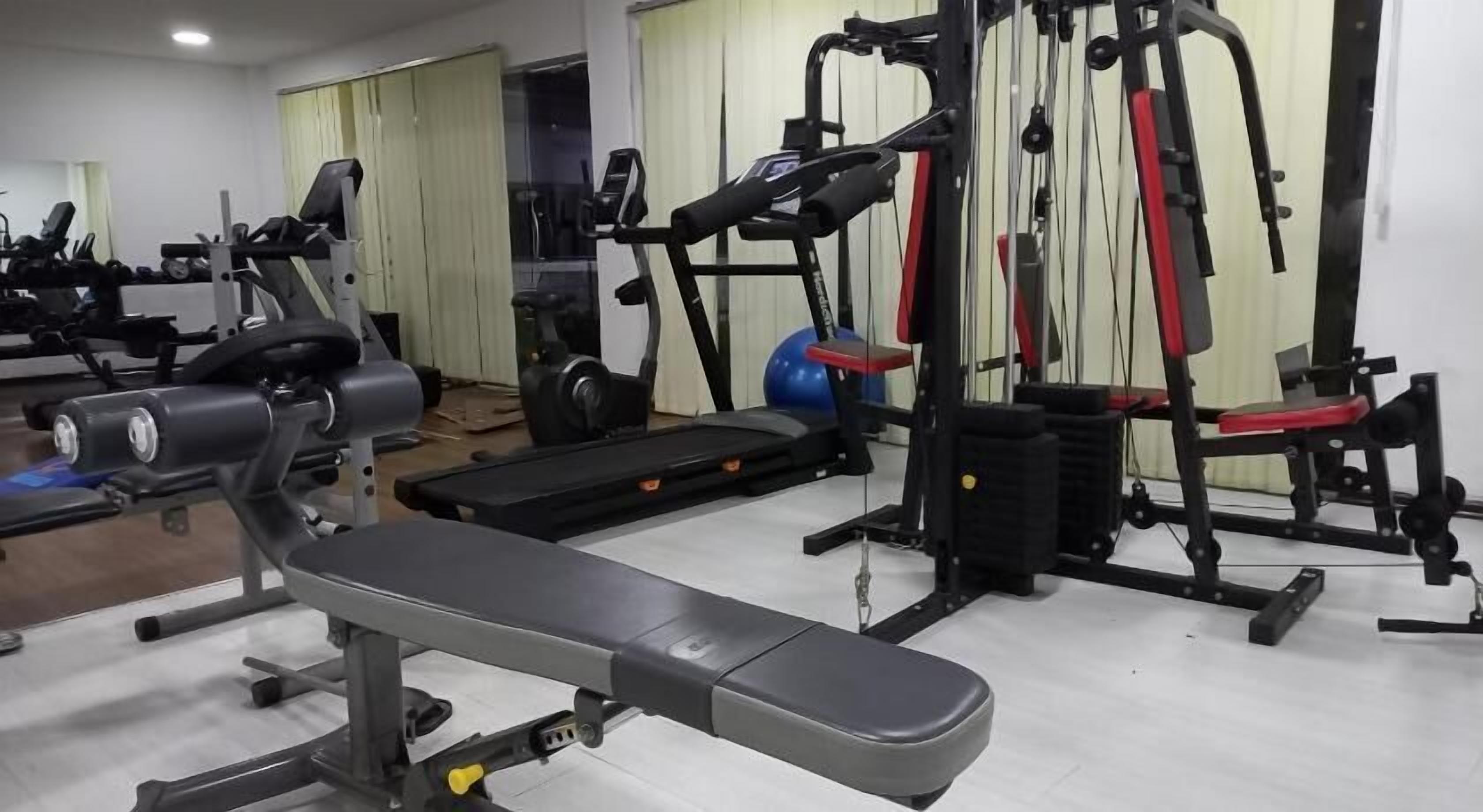 Een sportschool met diverse fitnessapparaten, waaronder een bank, krachtapparaten en een loopband.