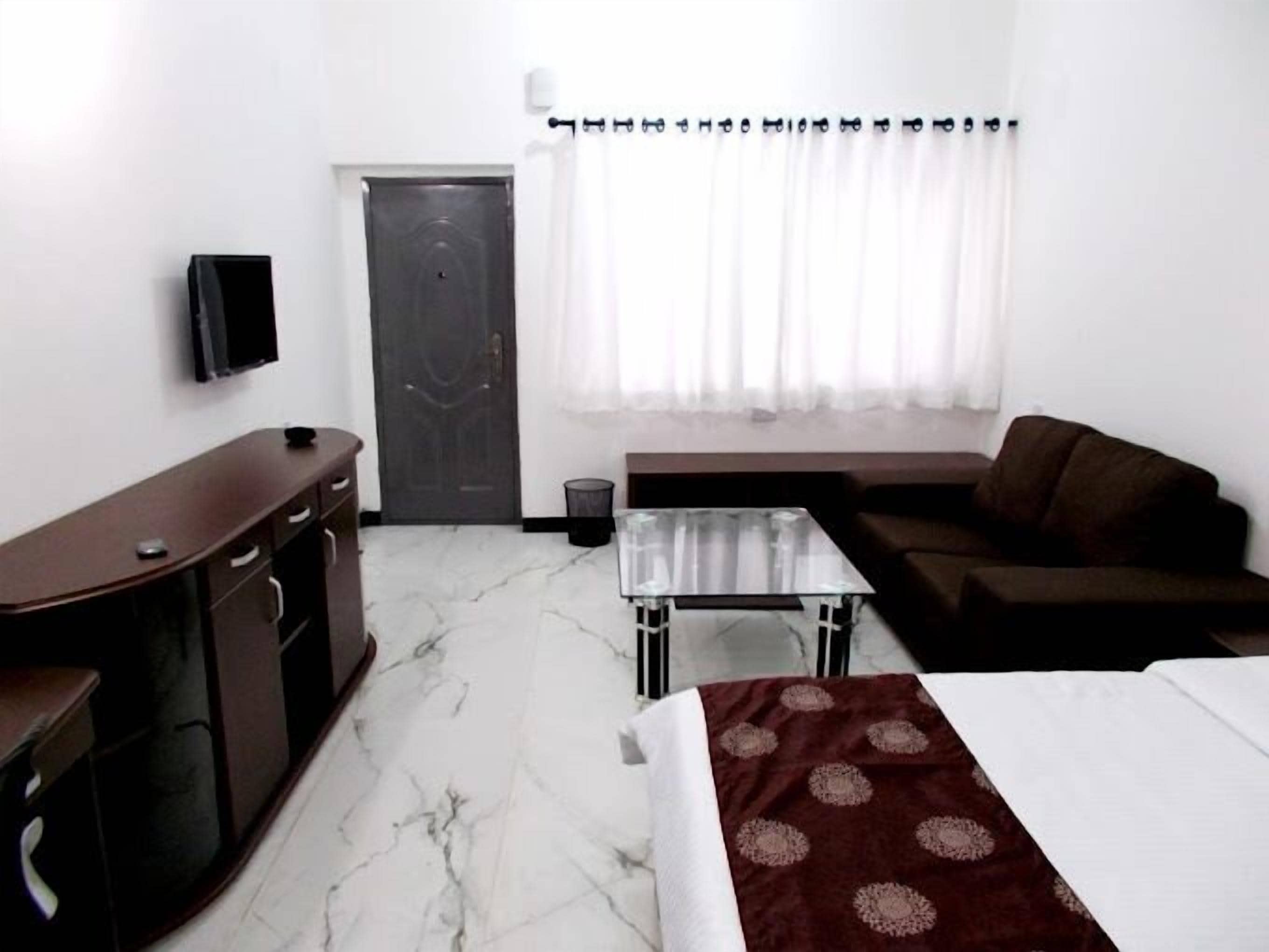 A hotel room with a bed, a sofa, a desk, a TV, and a window with curtains.