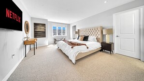 A bedroom with a large bed, a TV mounted on the wall, a window, and a door. - Lavish Home on Hamilton Mountain- King Bed (Hamilton)