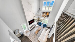 A modern living room with a white sofa, a coffee table, and a chandelier. There is a fireplace and a TV screen displaying Netflix. - Lavish Home on Hamilton Mountain- King Bed (Hamilton)