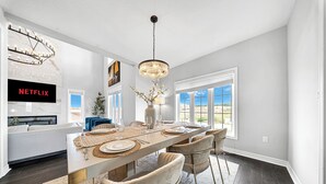 A modern dining area with a long table, multiple chairs, a chandelier, and a large window with a view. - Lavish Home on Hamilton Mountain- King Bed (Hamilton)