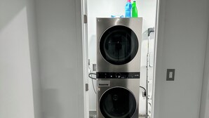 Pesuhuoneessa on kaksi päällekkäin asennettua, edestä täytettävää pyykinpesukonetta, ovi, joka johtaa toiseen huoneeseen, ja puulattia.