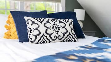 A bed with a white and blue patterned bedspread, two pillows with a black and white pattern, and a yellow throw pillow.