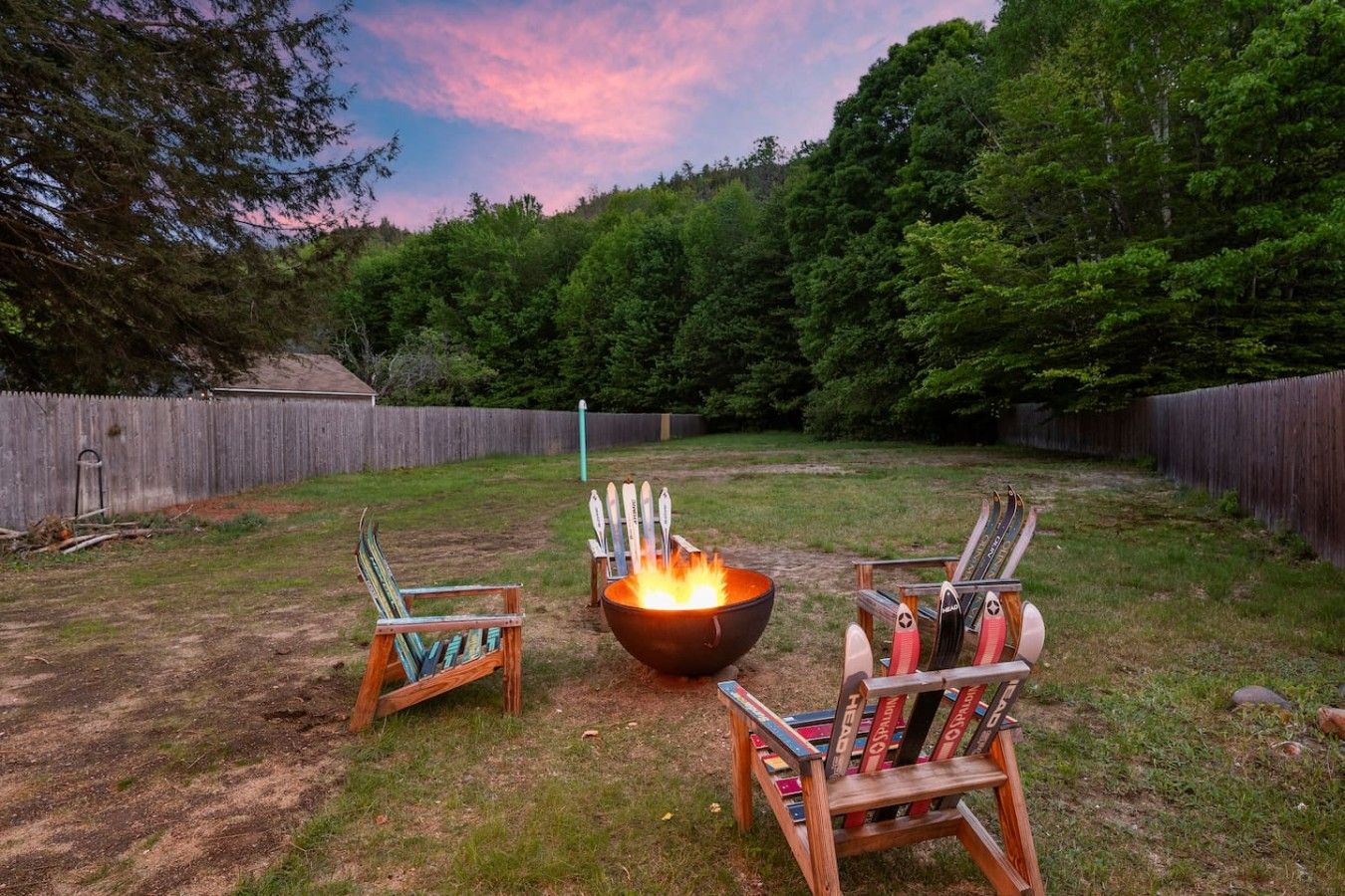 A backyard with a fire pit, two Adirondack chairs, and a wooden fence.