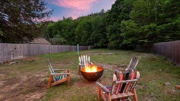 A backyard with a fire pit, two Adirondack chairs, and a wooden fence.