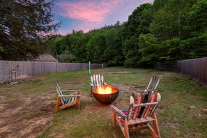 Un jardin avec un foyer, deux fauteuils Adirondack et une clôture en bois.
