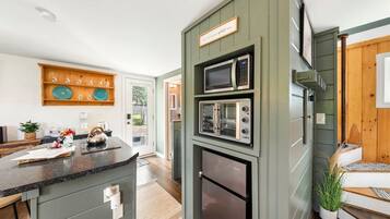 A kitchen with a built-in microwave, oven, and refrigerator, a wooden shelf with dishes, and a sign above the microwave.