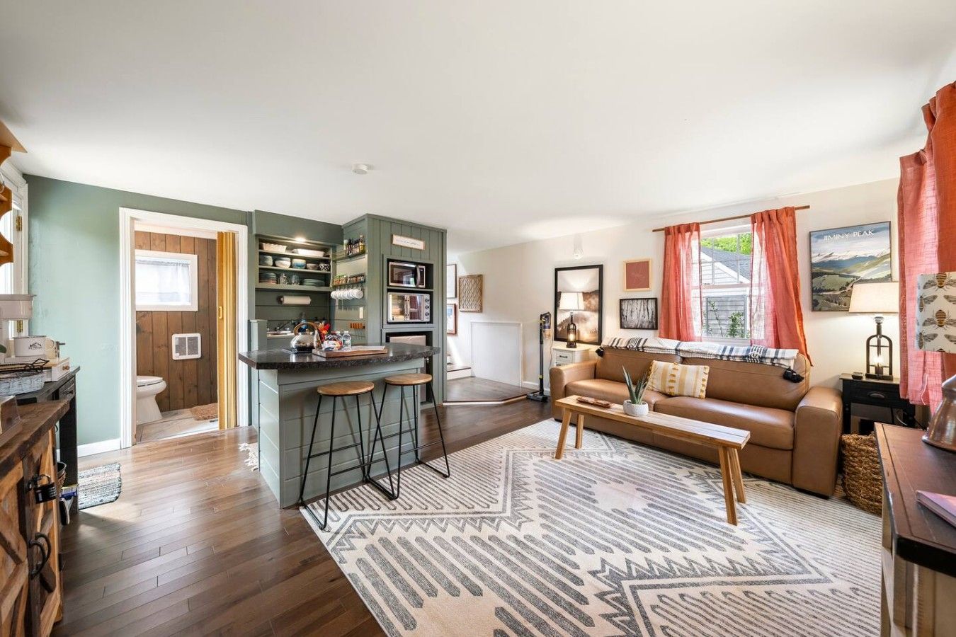 A modern living room with a brown sofa, a coffee table, and a kitchen area with a bar stool.