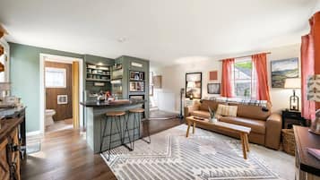 A modern living room with a brown sofa, a coffee table, and a kitchen area with a bar stool.
