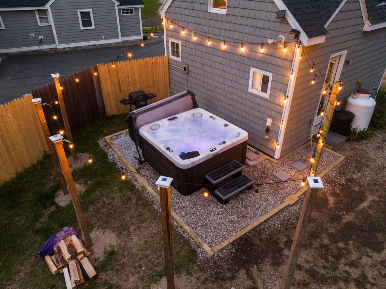 Ein Garten mit Whirlpool, Holzterrasse und Lichterketten.