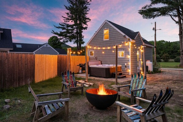 A cozy backyard with a fire pit, seating, and a hot tub.
