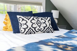 A bed with patterned pillows, a window with a view, and a lamp on a bedside table.