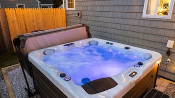 A hot tub with a wooden deck, a wooden fence, and a house in the background.