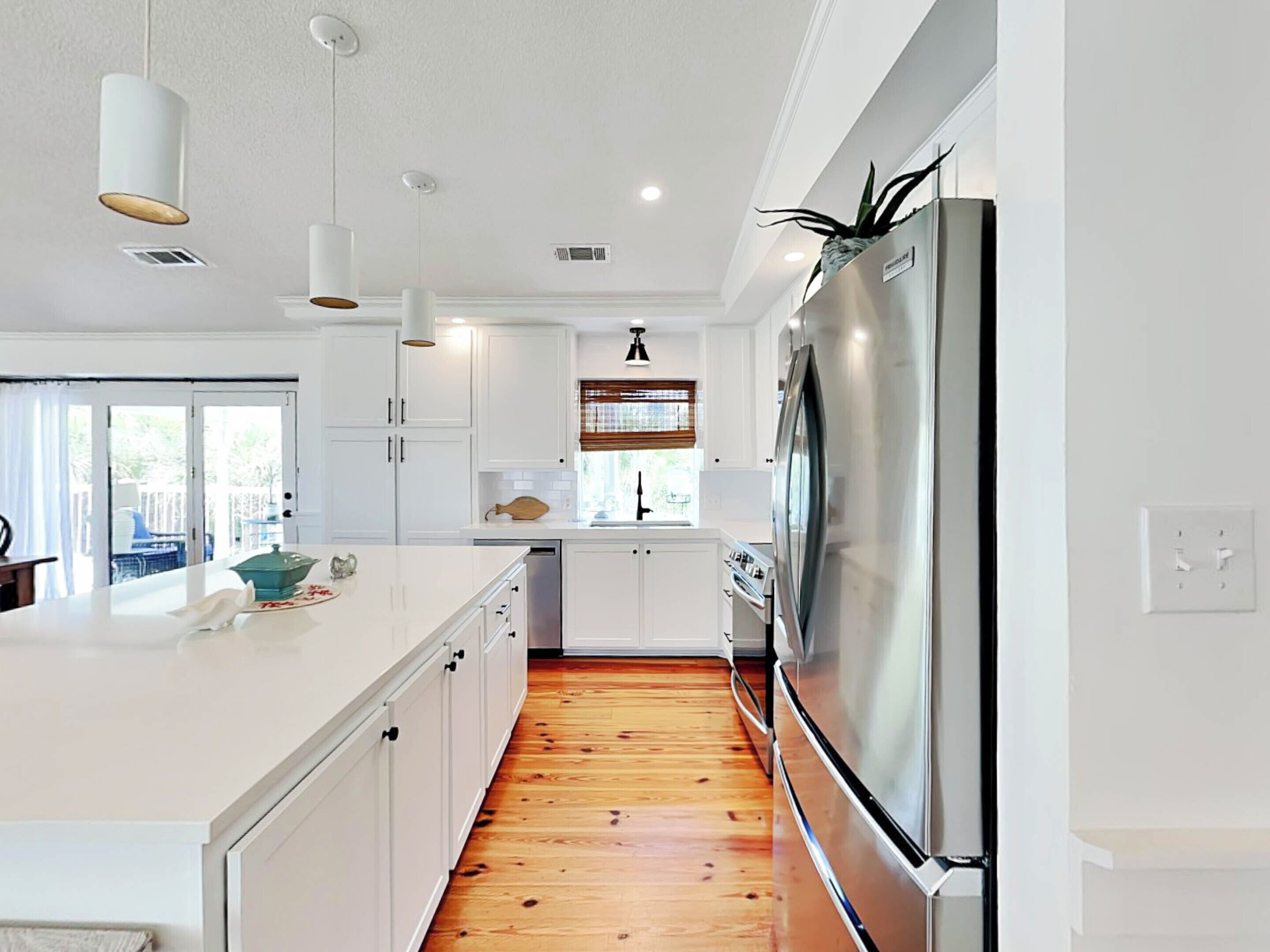 A modern kitchen with white cabinets, a stainless steel refrigerator, and a wooden floor.