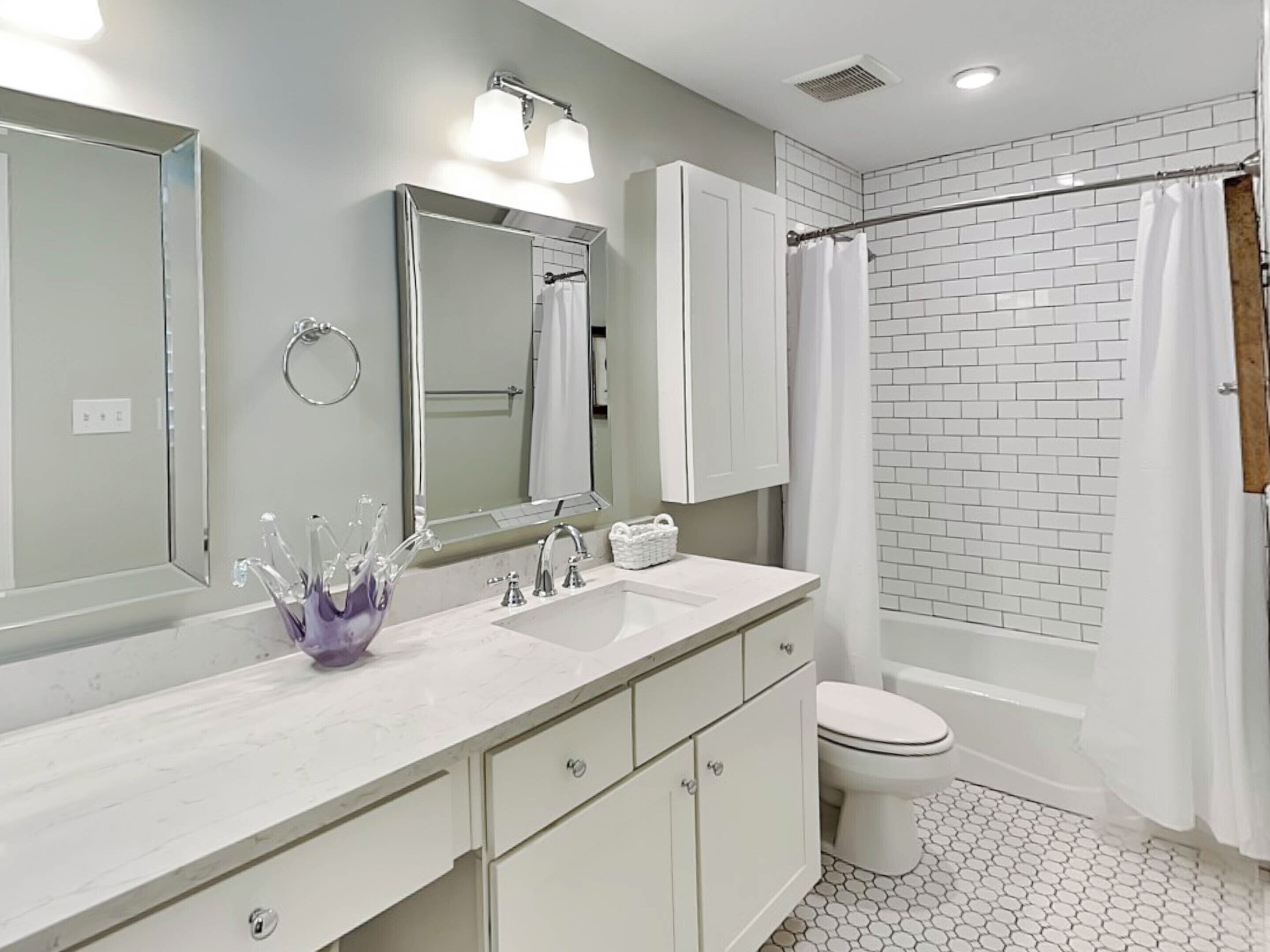 A bathroom with a white sink, mirror, and cabinet, a toilet, and a shower with a white curtain.