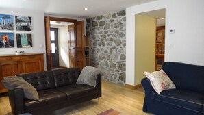 A living room with a dark leather sofa, a blue sofa, and a stone wall. There is a wooden cabinet and a door leading to another room. - Spacious 5-bedroom house in enchanting Luz-Saint-Sauveur 
 (Luz-Saint-Sauveur)