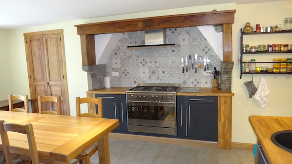 A kitchen with a central island, wooden chairs, a stove, and a variety of kitchen utensils on the wall.