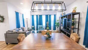 Ein Essbereich mit einem Holztisch, gemusterten Stühlen, einem blauen Sofa und einem Bücherregal mit Pflanzen.