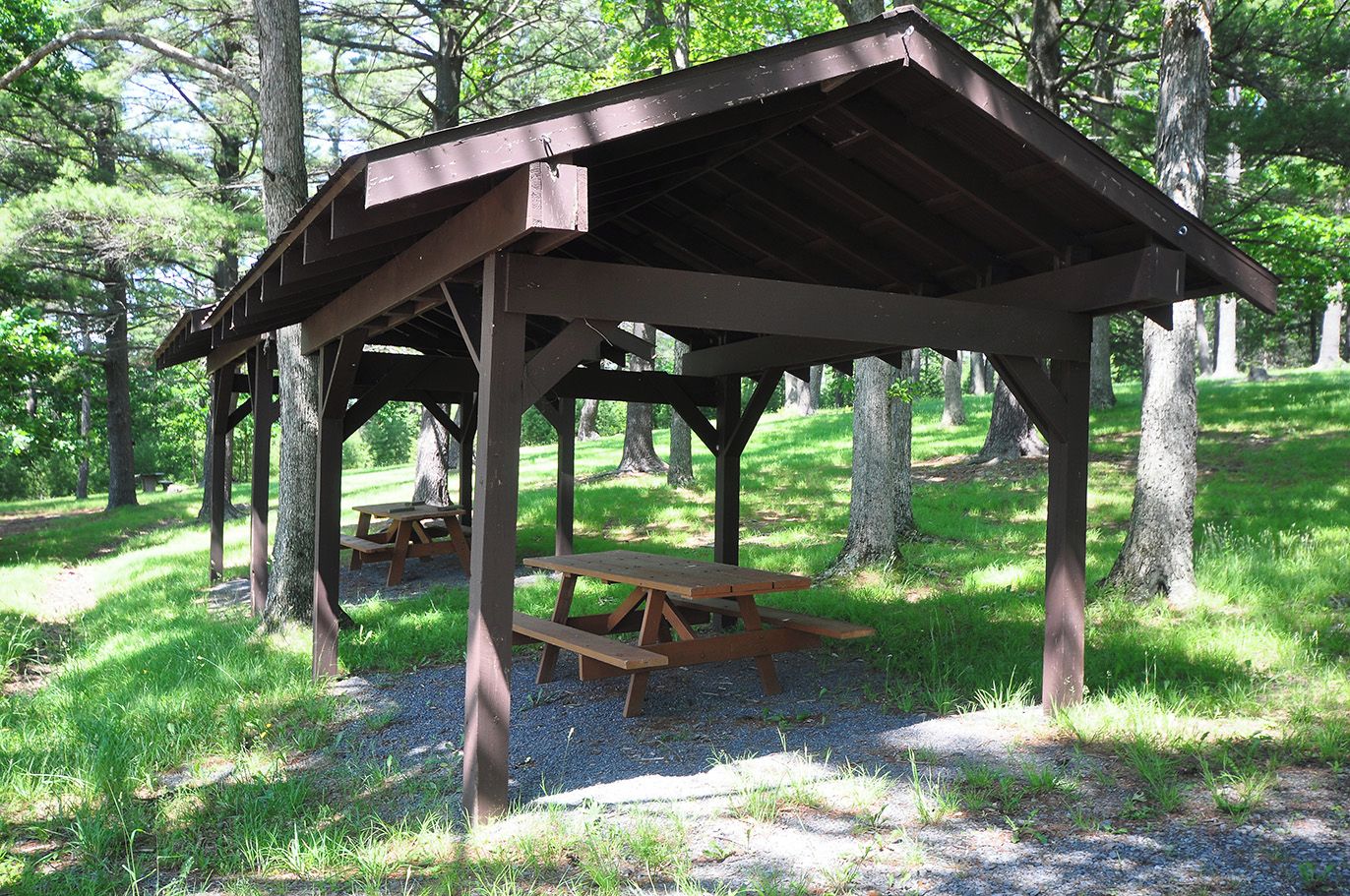 A wooden pavilion with picnic tables in a forested area.