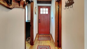 A wooden hallway with a red door, patterned rugs, and a wall-mounted decoration of a bear and trees. - Cooper's Landing by Taylor Made Deep Creek (Swanton)
