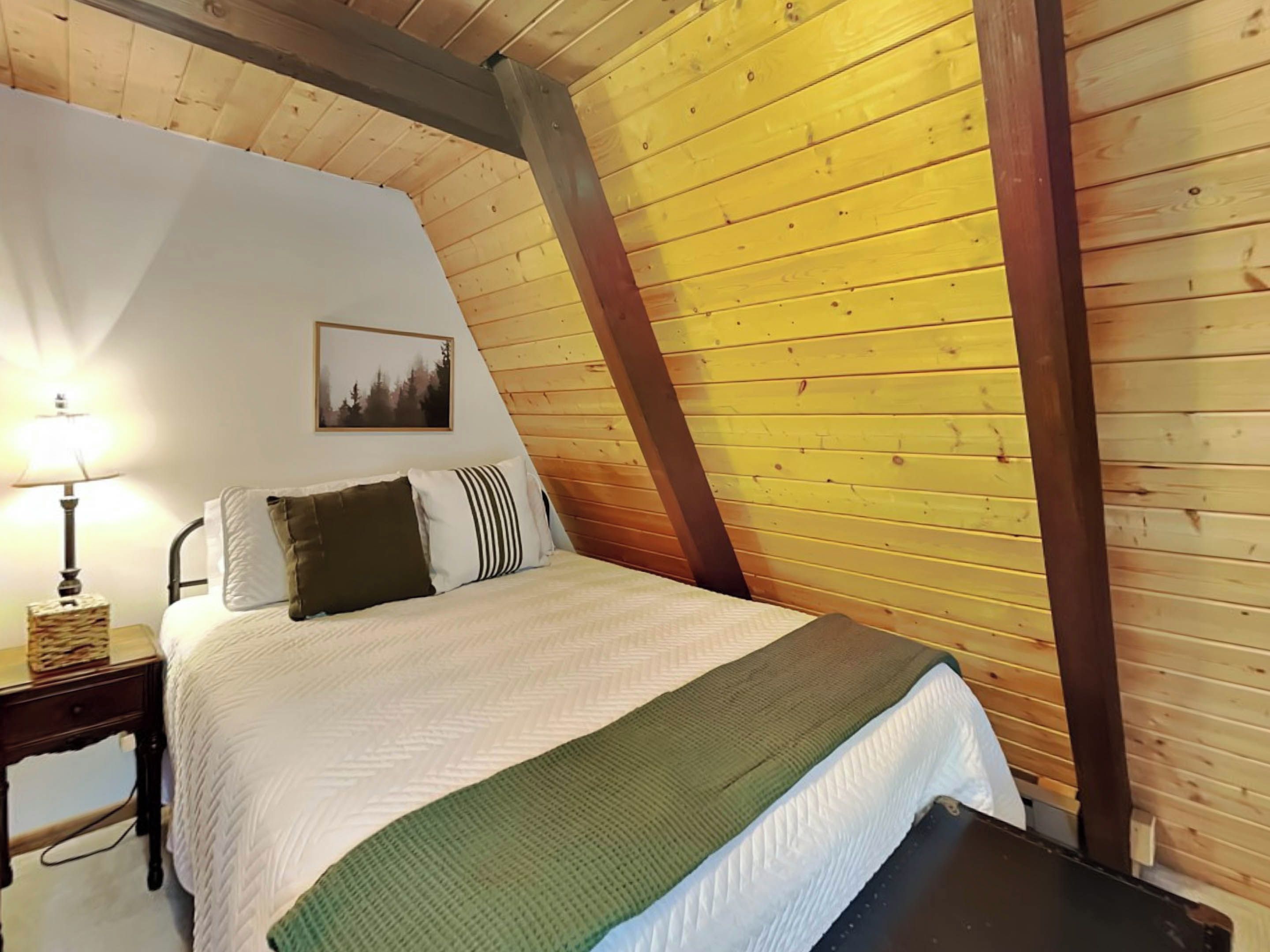 Een slaapkamer met een bed, nachtkastje, lamp en een ingelijst schilderij aan de muur.