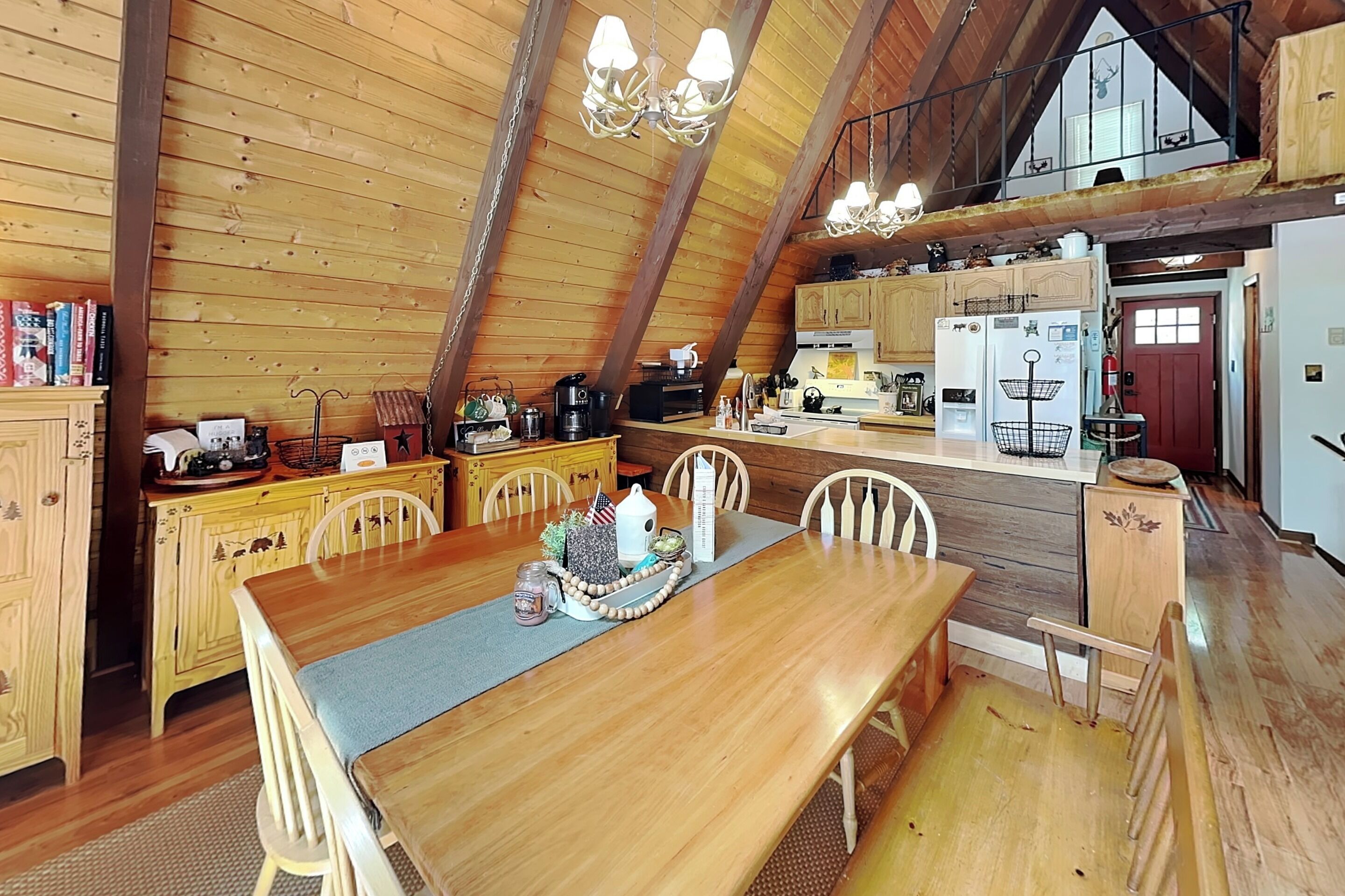 A wooden interior with a dining table, chairs, a kitchen area, and a loft space.