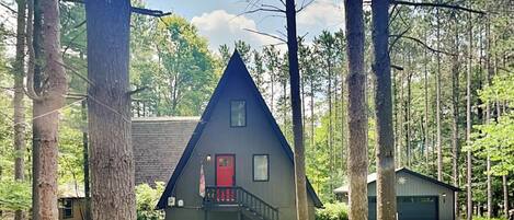 A cabin with a red door, a small porch, and a garage.